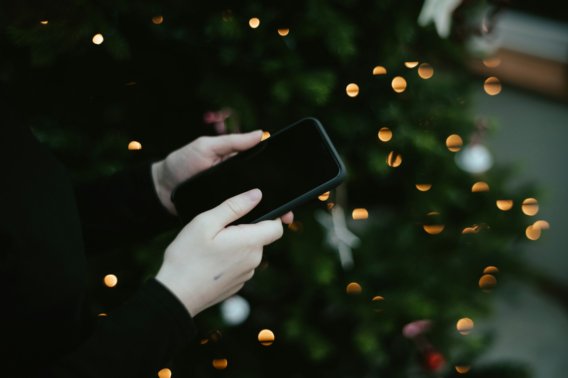 Person holding a phone with Christmas lights in the background