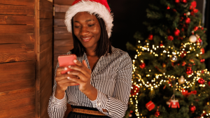 Young woman standing by the Christmas tree and using smart phone